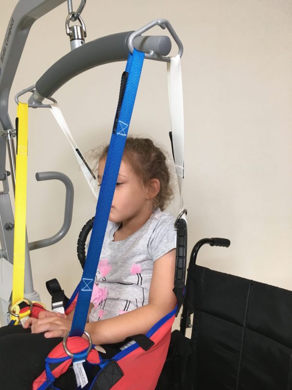 Young disabled girl being moved in ProMove sling with yellow and blue straps attached to the hoist