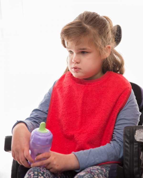 Disabled girl wearing Seenin bib apron in red