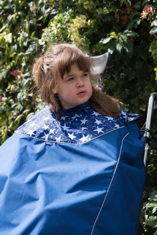 Disabled girl in navy Seenin total waterproof wheelchair cover with white star pattern