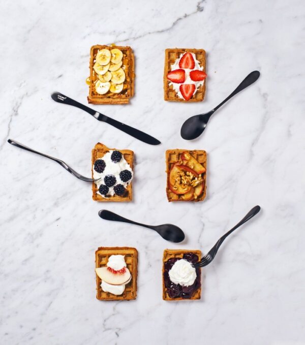 Image is a photograph of 6 square plates of food on a marble surface with Matt Black Knork cutlery