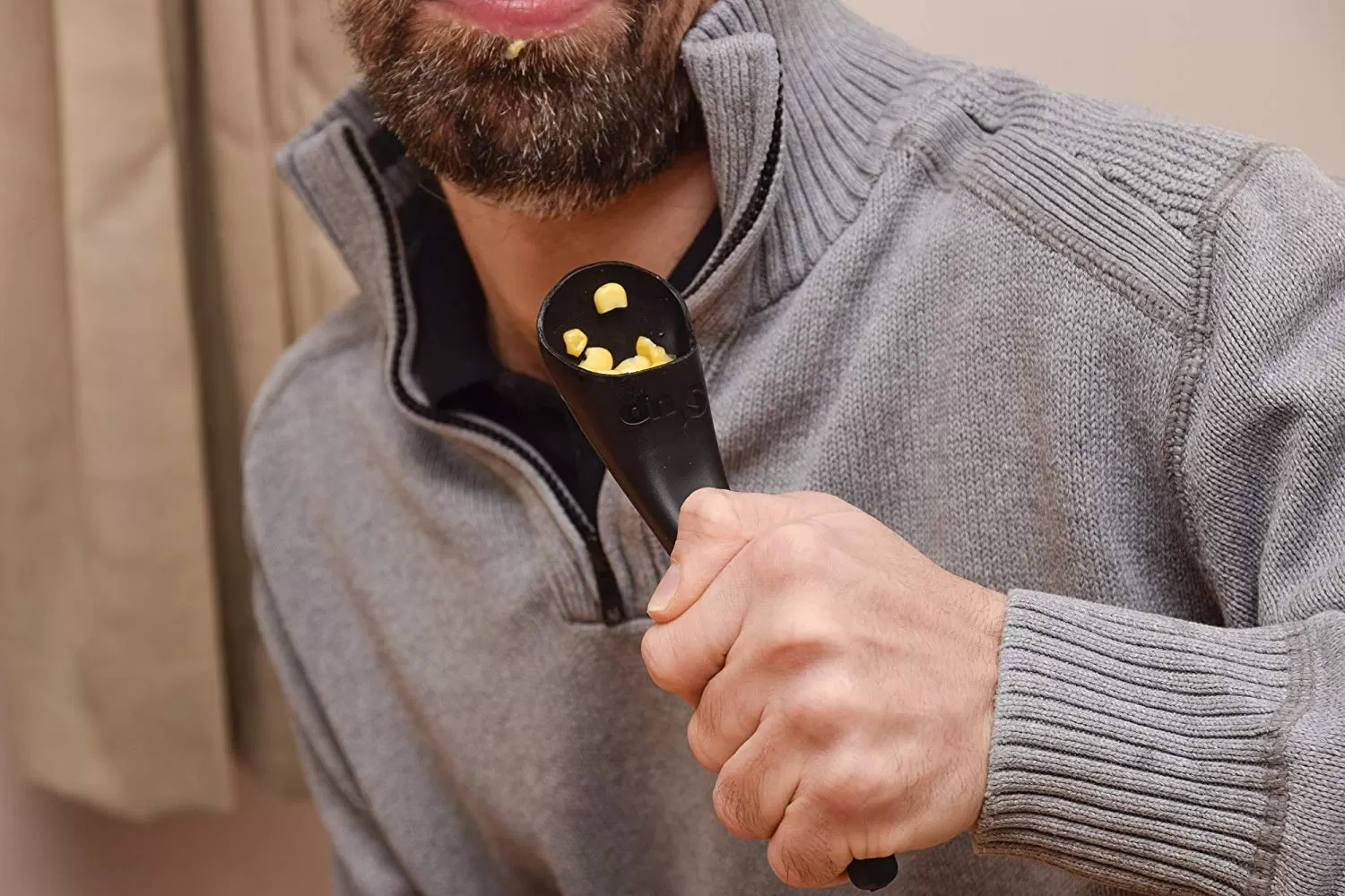 Image is a photograph of a man holding a S'Up Spoon filled with sweetcorn, poised, ready to eat