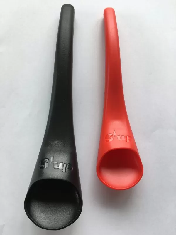 Image is a photograph of a black, standard-sized S'up Spoon lay on a white surface next to a red, S'up Spoon Mini