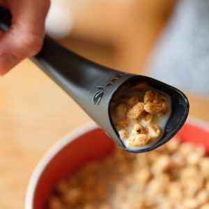 Image is a photograph showing the S'up Spoon filled with milk and cereal, poised over a red bowl with cereal in it