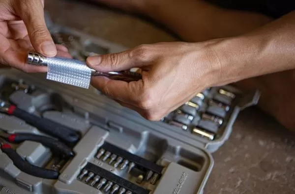 Image is a photograph of someone placing a strip of Cat Tongue Grip Tape to the handle of a tool from a tool kit