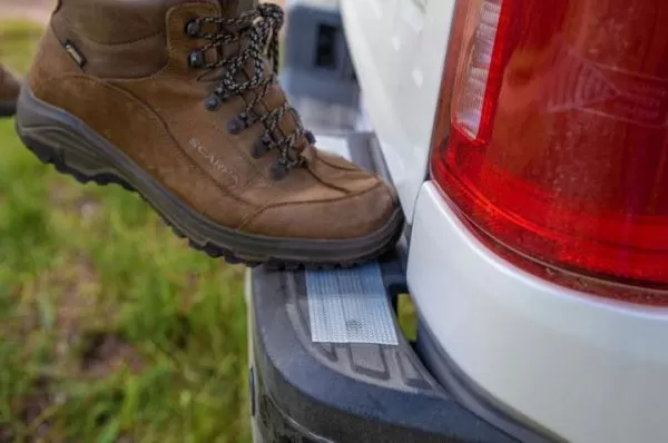 Image is a photograph of a boot standing on a strip of Cat Tongue Grip Tape that has been attached to the back footplate of a vehicle