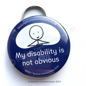 Image is a photograph of a blue, round keyring with a smiling stickman illustration, with text which reads: "My disability is not obvious"