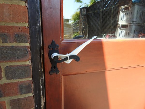 Image is a photograph of the exterior of a backdoor with a black, metal level handle with a Tru Grip handle extender attached