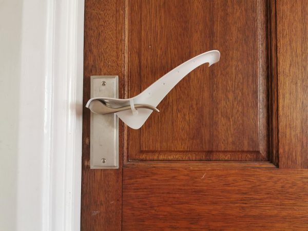 Image is a photograph of a wooden, varnished door with a brushed steel level handle, with a Tru Grip door handle extender attached