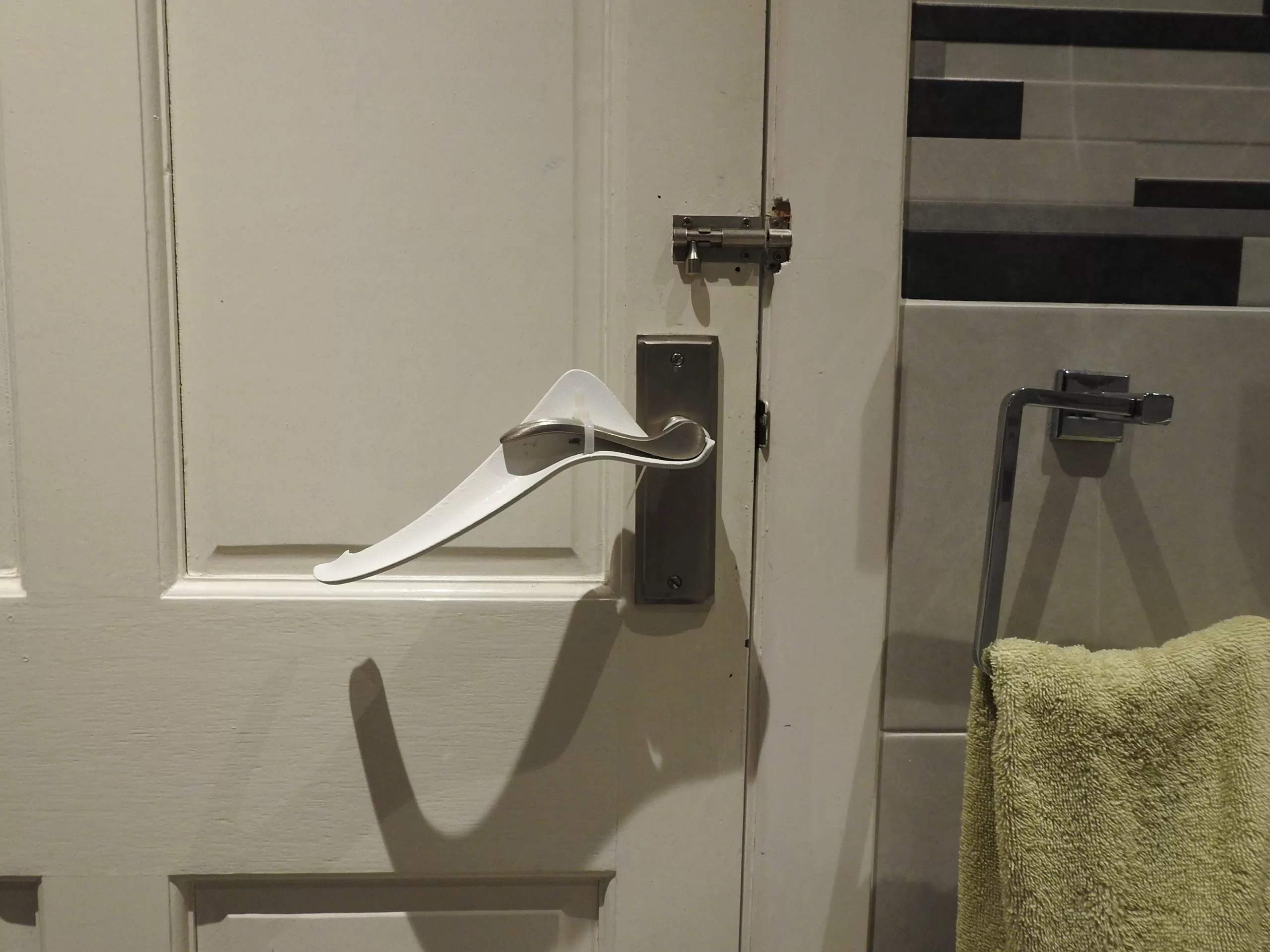 Image is a photograph of a white internal house door with a Try Grip handle extension kit installed upside down to aid those with arthritis