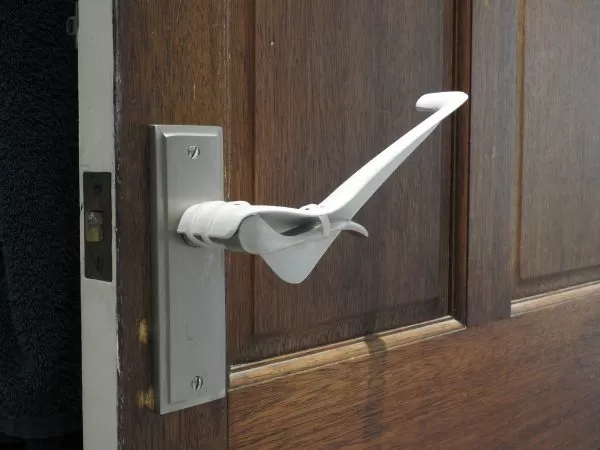 Image is a photograph of a brown wooden internal house door with a Tru Grip door handle extension kit installed