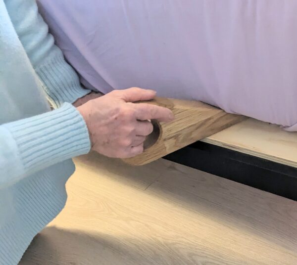 bed wedge mattress lifter being shown inserted under the mattress tucking in sheets