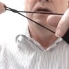 Image is a photograph of a middle-aged man stretching the ear straps of the lip reading mask and adjusting the length using the plastic ferrule