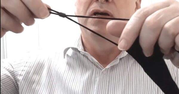 Image is a photograph of a middle-aged man stretching the ear straps of the lip reading mask and adjusting the length using the plastic ferrule
