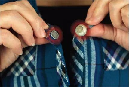 Image is a photograph of the close-up of the neck of a man wearing a blue, checked shirt fitted with magnetic buttons