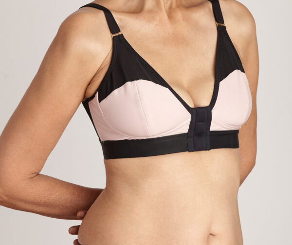 Image is a front view of a lady wearing an Elba London front-fastening, magnetic, adaptive bra in blush pink cotton and black mesh