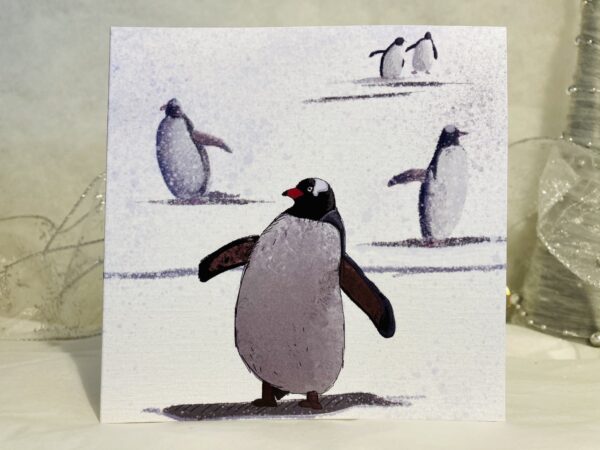 Image is a photograph of a penguin art christmas card illustrated with serveral pengiuns waddling through a snowy landscape