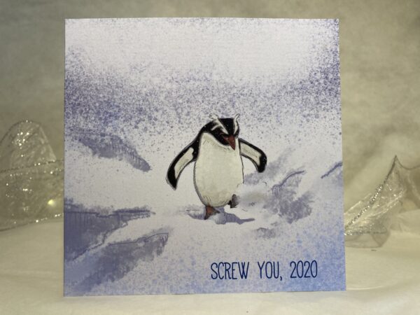 Image is a photograph of an illustrated christmas card featuring a penguin kicking through the snow, with text which reads: "SCREW YOU, 2020"