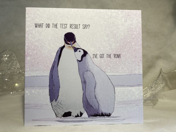 Image is a photograph of an illustrated card featuring a baby penguin looking up to their adult penguin. Text on card reads: "What did the test result say? I've got the 'Rona"