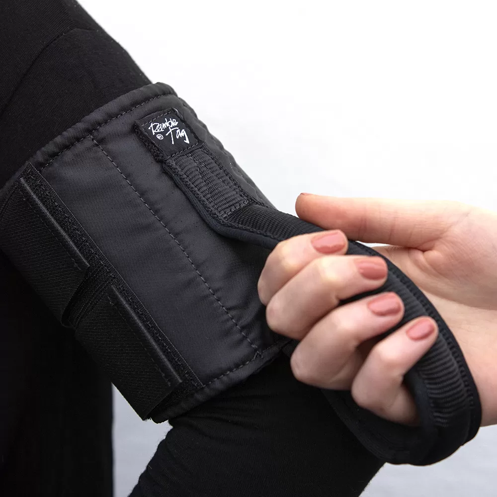 Image is a photograph of a woman's hand with dusky pink painted nails, gripping the guidance handle of a Ramble Tag worn around the top of a guide's arm