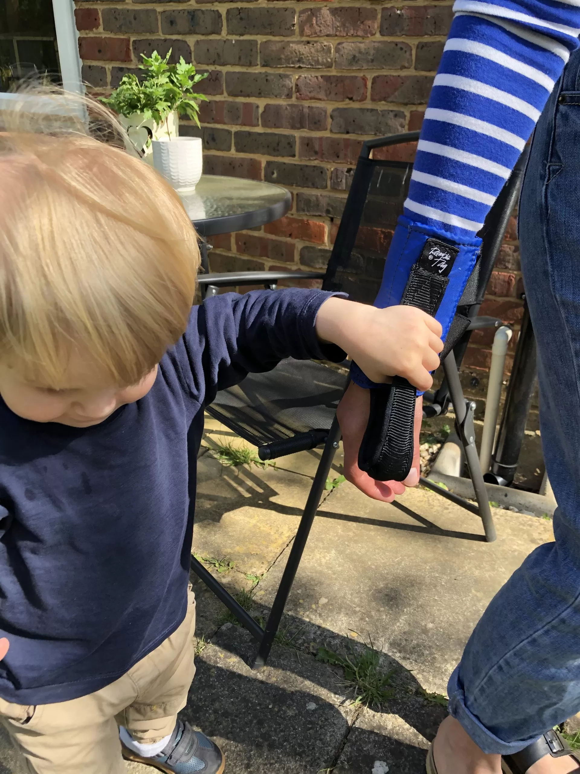 Image is a photograph of a toddler boy with blonde hair holding the strap of a Ramble Tag on a guide's arm