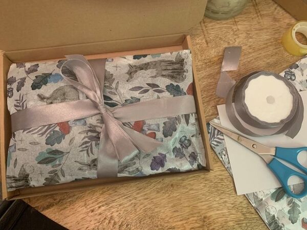 Image shows a pretty, gift wrapped package on a wooden table, with scissors and ribbon to one side