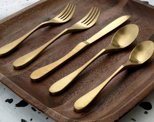 Satin brass Knork knife and fork 5-piece cutlery set on a wooden board