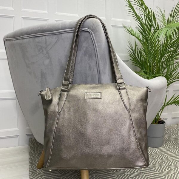 Image is a photograph of a Samantha Renke accessible handbag in Metallic Grey hung over the back of a grey velvet armchair in a modern living room