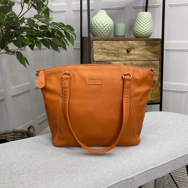 Image is a photograph of a Samantha Renke accessible handbag in Burnt Orange on a table in a living room