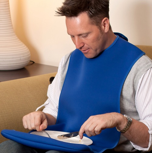 A man sat eating wearing a Care Design's adult tabard-style clothing protector in blue