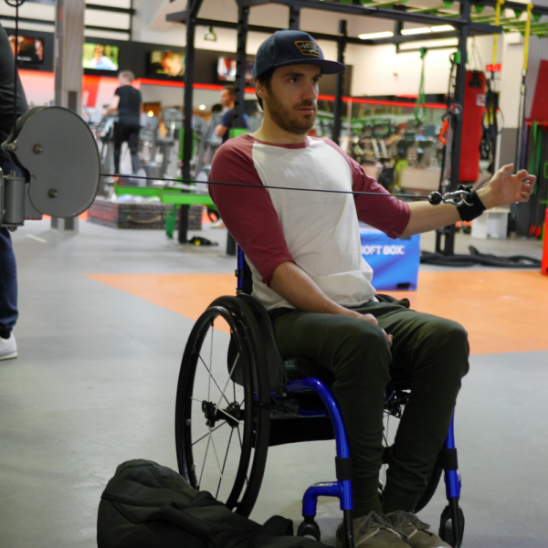 Man in a wheelchair in a gym, using the d ring aid to pull an exercise rope.