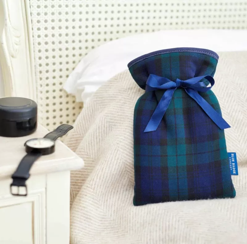 Black watch mini water bottle on a white bed. A watch sits on the bedside table