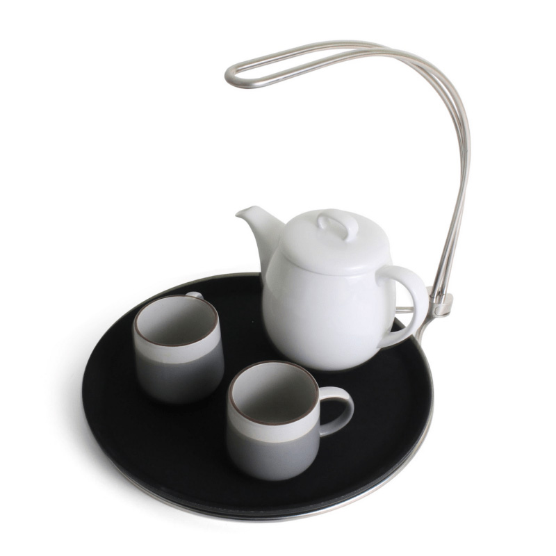 Image is a photograph of the one-handed, no-spill Tipsi Tray with a teapot and two cups on the tray surface, on a white background