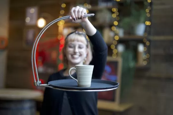 A lady holding the tipsi tray in one hand up to the camera. A mug sits atop the tray.