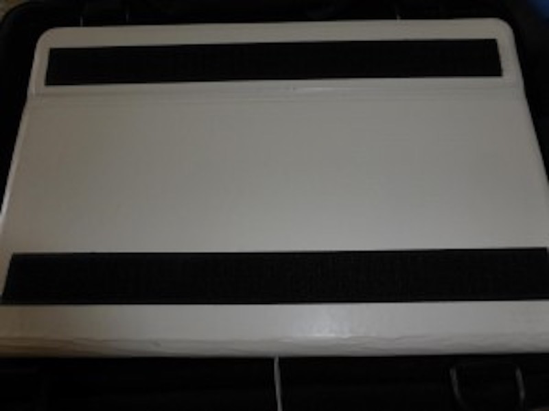 Back of a white tablet computer case, with two parallel strips of black adhesive hook tape on the back.