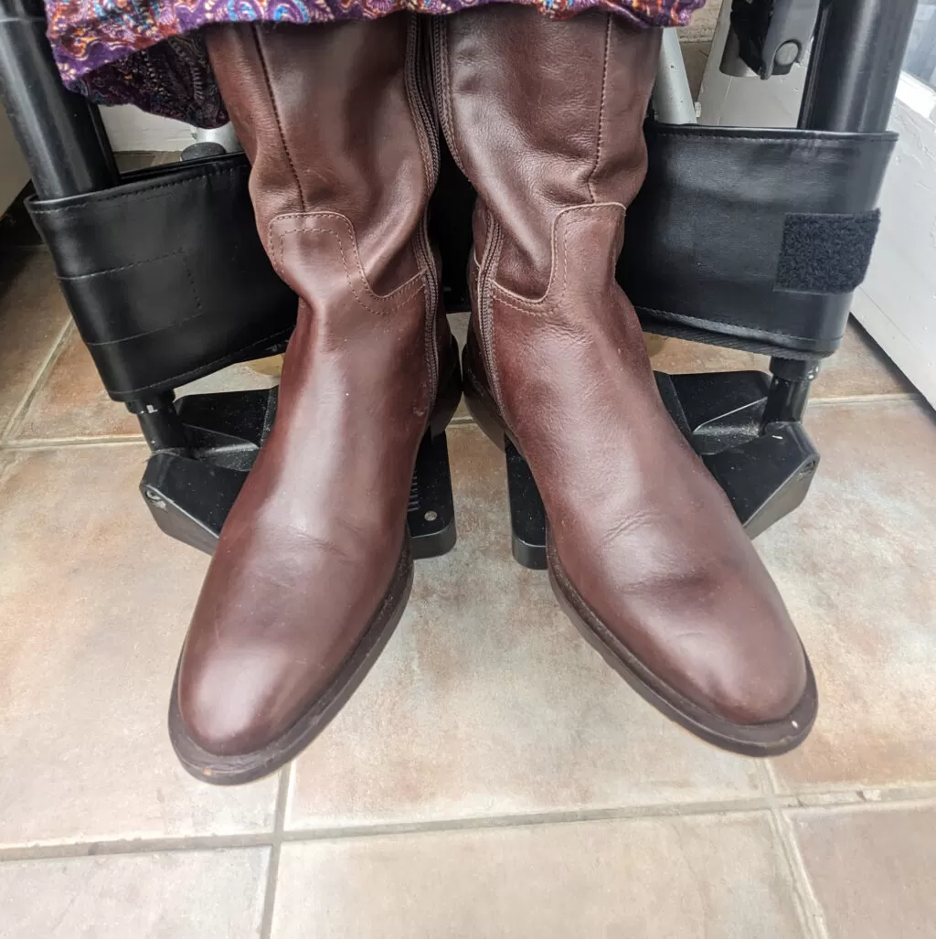 Black wheelchair leg strap behind two brown boots on an electric power wheelchair