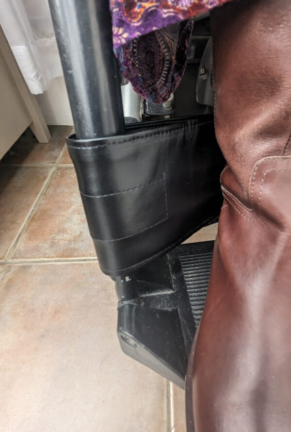 Black wheelchair strap for legs with a brown boot on fooytplates of a powerchair, the strap can be seen at the ankle height keeping the feet on the footplate