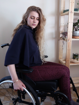 l able unisex jersey cape in navy being worn by a blonder girl sitting in her wheelchair