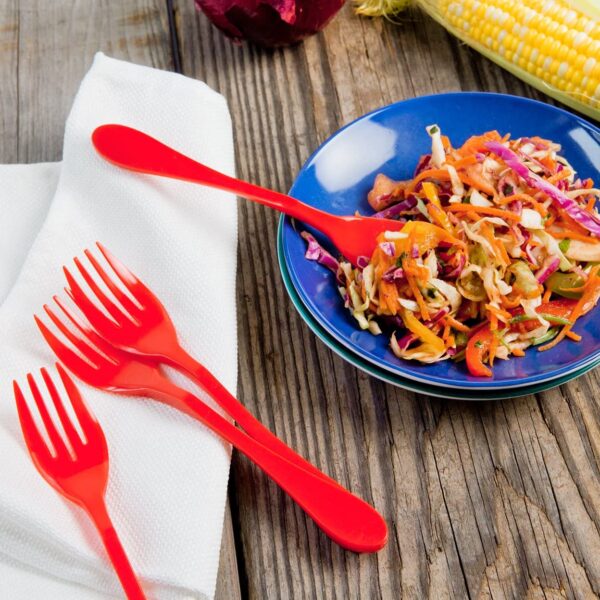 The Knork plasticware is red sitting on a wood table. One red knork plastic ware sticks out of a tasty looking meal