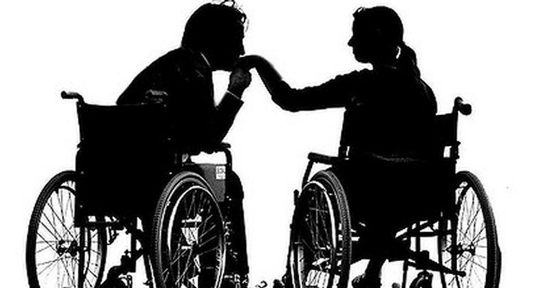 Sillohette image of man kissing woman's hand. They are both in wheelchairs
