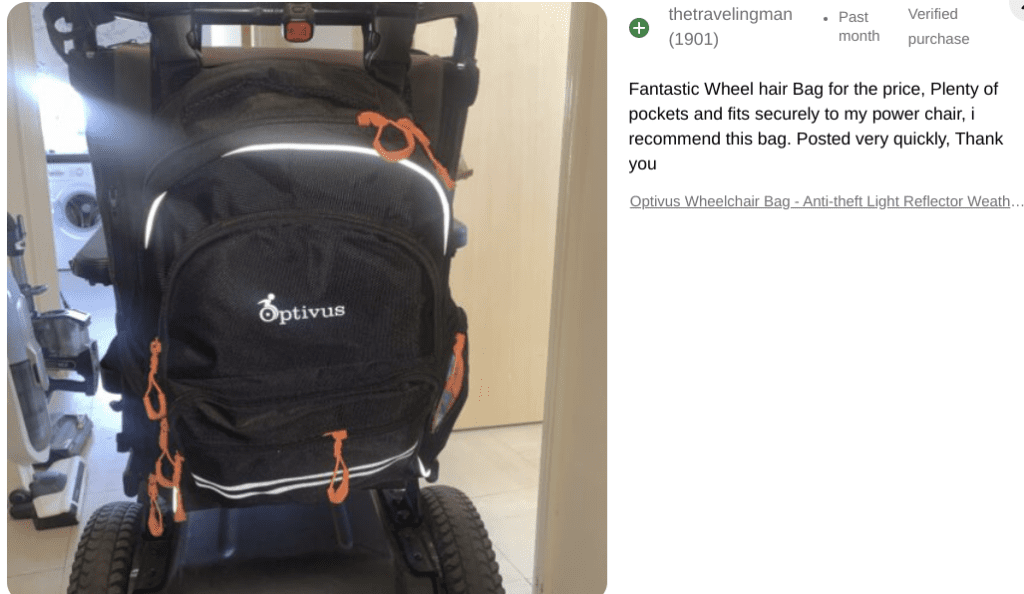 A black Optivus wheelchair bag with multiple pockets and bright orange zippers is attached to the back of a power chair. The bag has reflective strips and a white Optivus logo