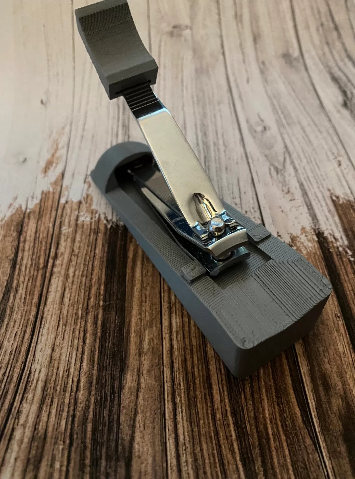 one handed nail clippers, grey base with the nail clippers set into them on a wooden table top