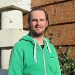 Bradley Cory, young bearded man in a green hoodie outside a university building