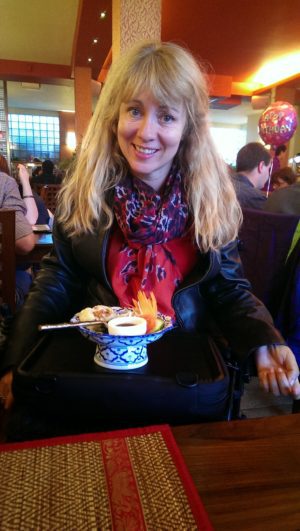 woman with blonde hair at a japanese resturant with a bowl of sushi on a trabasack mini tray