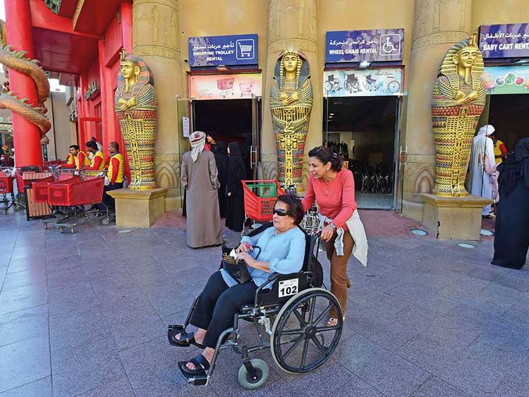 An older woman with sunglasses in a transport wheelchair in Dubai's Global Village Market