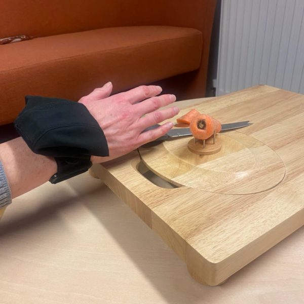 lite grip aid being shown by a person with poor grip using a knife to cut a carrot on a chopping board