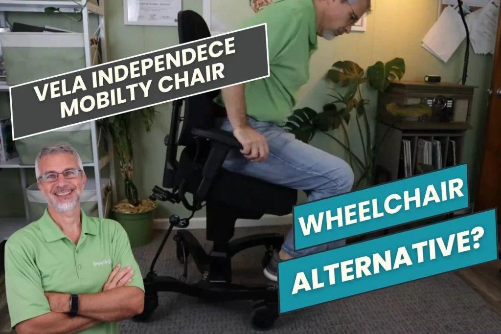 A man in a green shirt is smiling and standing with arms crossed in the foreground, while another man is seated and leaning forward on a VELA Independence Mobility Chair in the background. Text overlays read "VELA Independence Mobility Chair" and "Wheelchair Alternative?" The room features plants, shelves, and soft lighting.