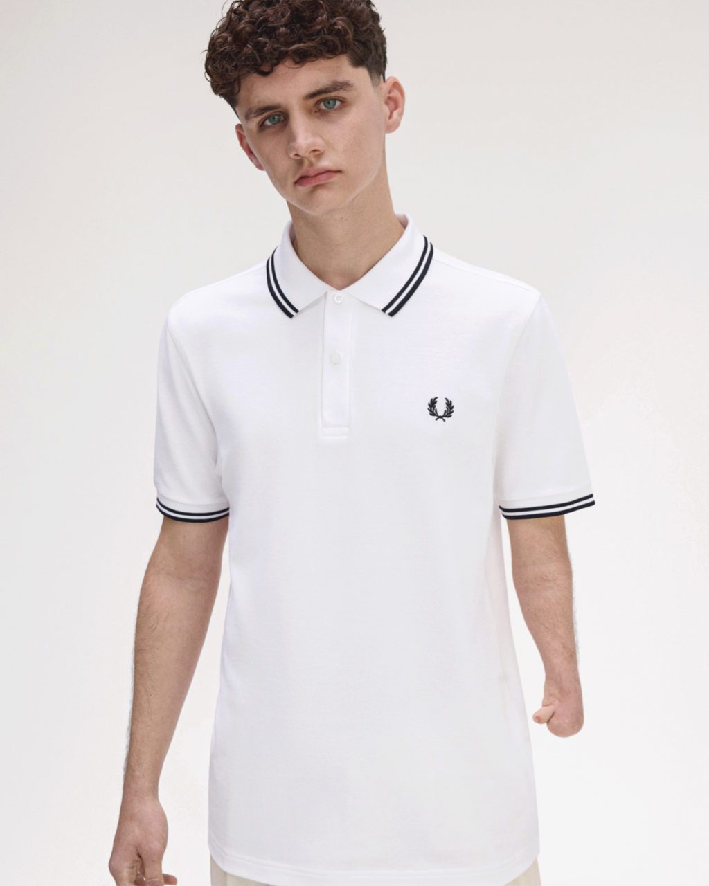 Young man with a limb difference wearing a white Fred Perry adaptive polo shirt with black twin tipping and laurel wreath logo.