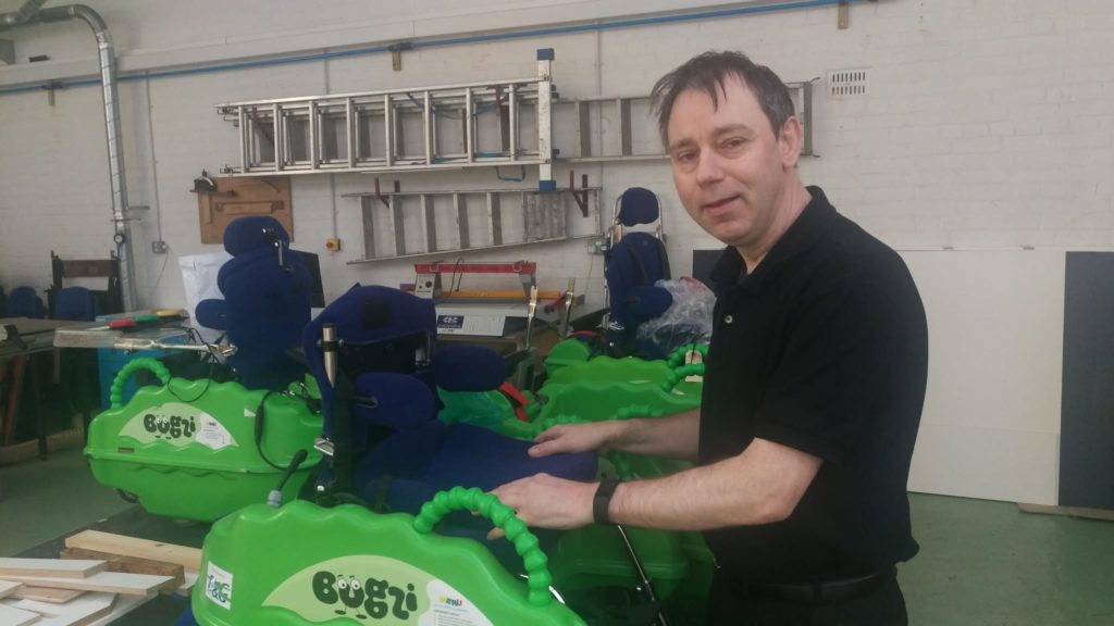 Engineer adjusting a Bugzi powered wheelchair for young disabled children in a workshop where several Bugzi units are being assembled.