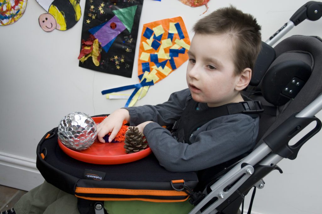 Child sitting in a supportive buggy using a Trabasack lap tray with sensory objects.