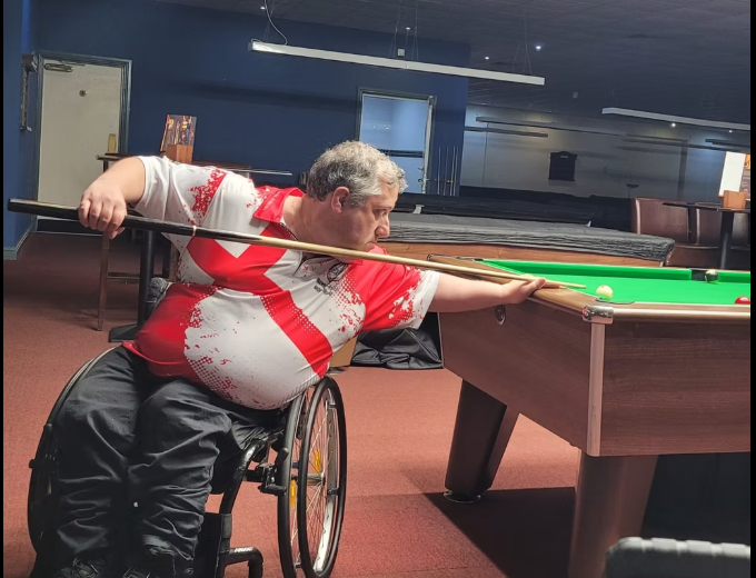 Gareth Clarke lines up a shot from his wheelchair at a pool table during a game.